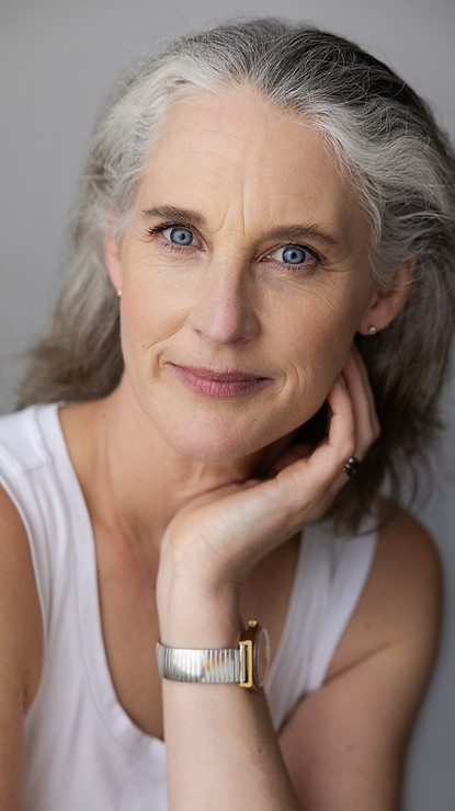 Head and shoulders of smiling woman with piercing blue eyes, silver hair, one hand cradling her cheek