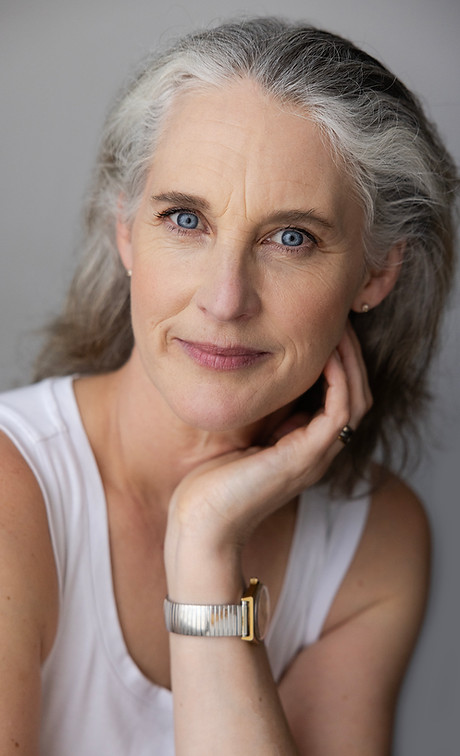 Head and shoulders of smiling woman with piercing blue eyes, silver hair, cradling cheek in palm of one hand