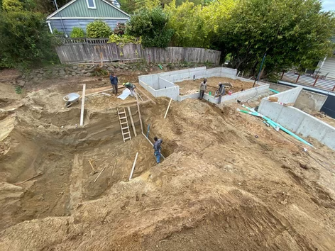 Excavation and foundation construction at residential housing site with workers and footings visible.
