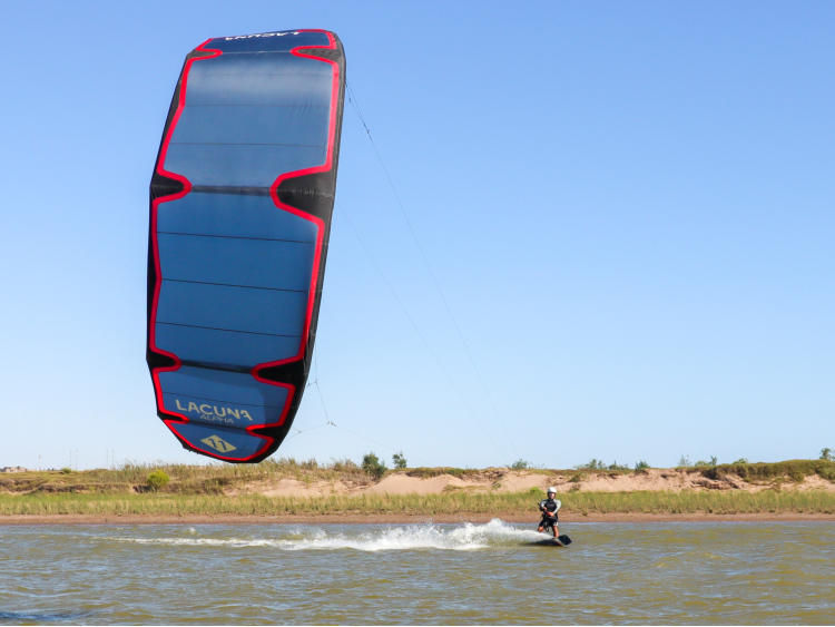 Thumbnail: Kitesurfer riding near water with Lacuna Alpha V4 and visible blue kite.