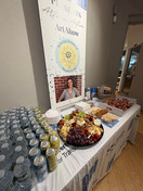 Table with bottled water, snacks, and table signage in an art gallery.