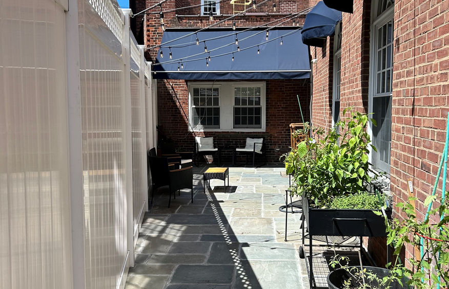 A charming brick-walled courtyard with string lights, potted plants, and cozy seating, creating a peaceful outdoor retreat.