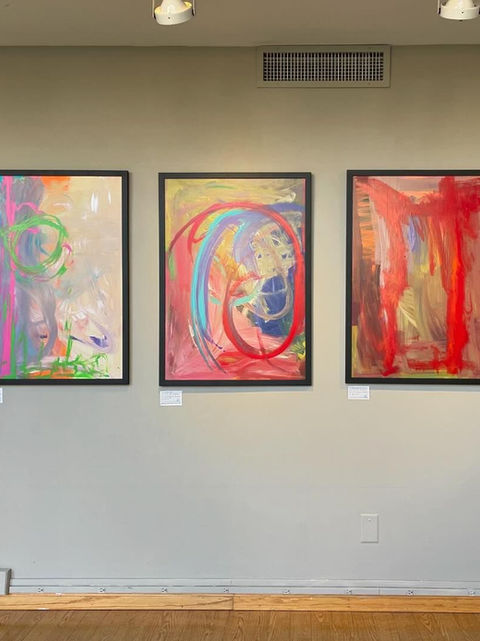 Framed abstract art pieces in red, blue, and green tones on a gallery wall.