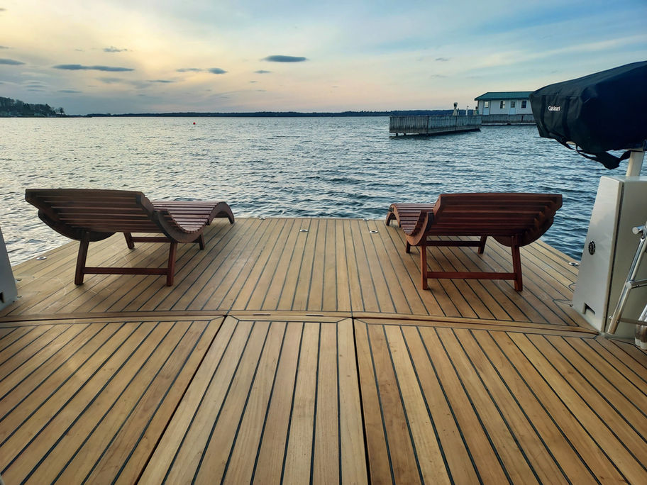 Two lounge chairs on a wooden dock overlooking the calm ocean waters.