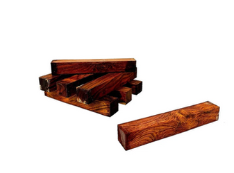 Several highly figured mahogany lumber pieces are stacked on white surface, close up.