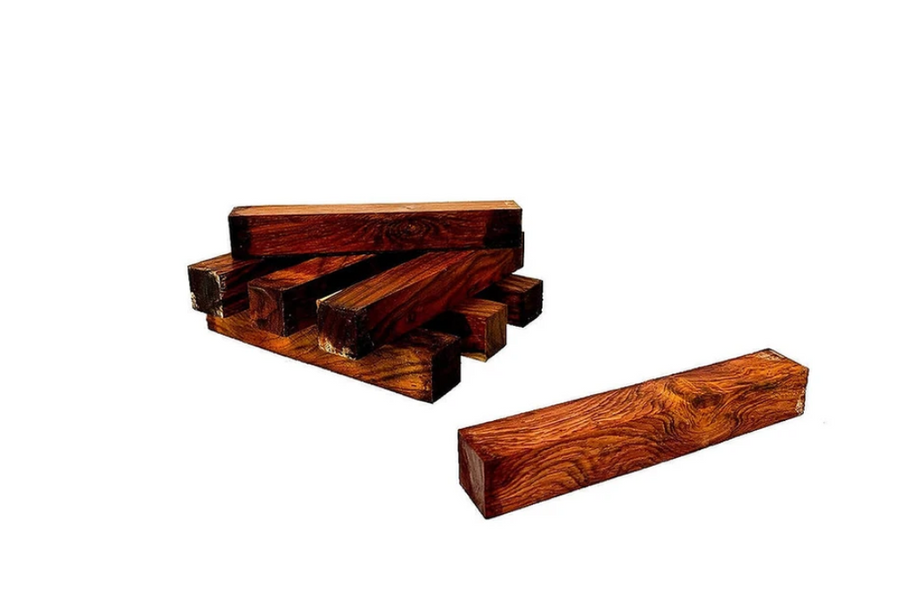 Several highly figured mahogany lumber pieces are stacked on white surface, close up.