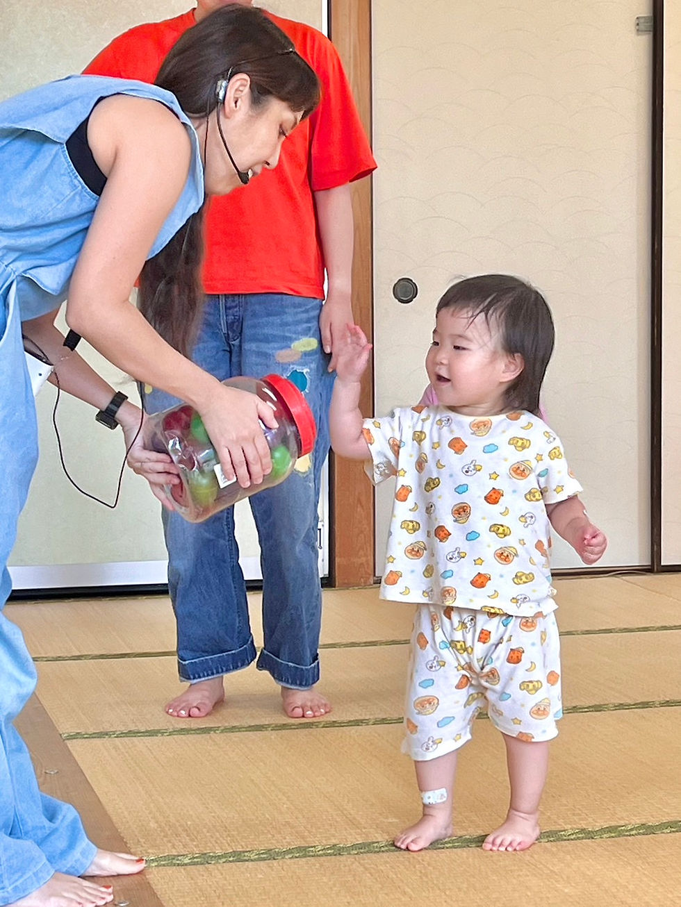 畳の部屋で、青い服の女性が赤いフタの瓶を差し出し、幼児が笑顔で手を伸ばしている。