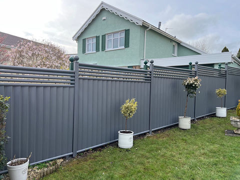 Modern grey metal garden fence with slatted top and potted plants.