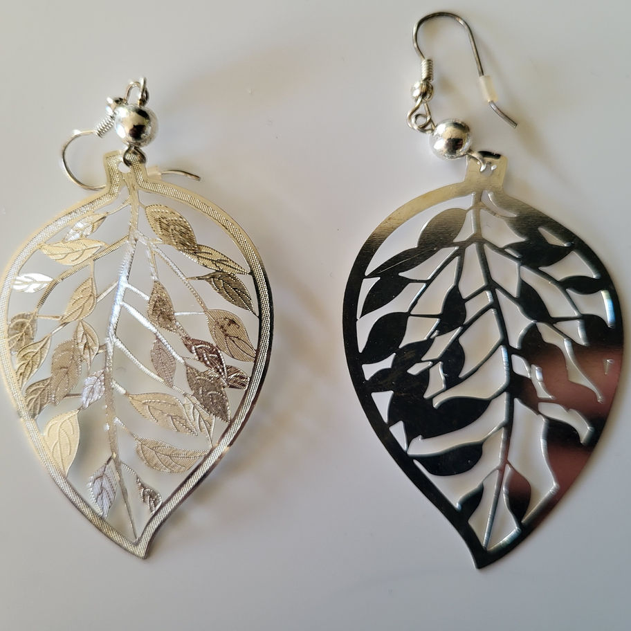 Deux boucles d'oreilles argentées en forme de feuilles découpées finement, élégantes.