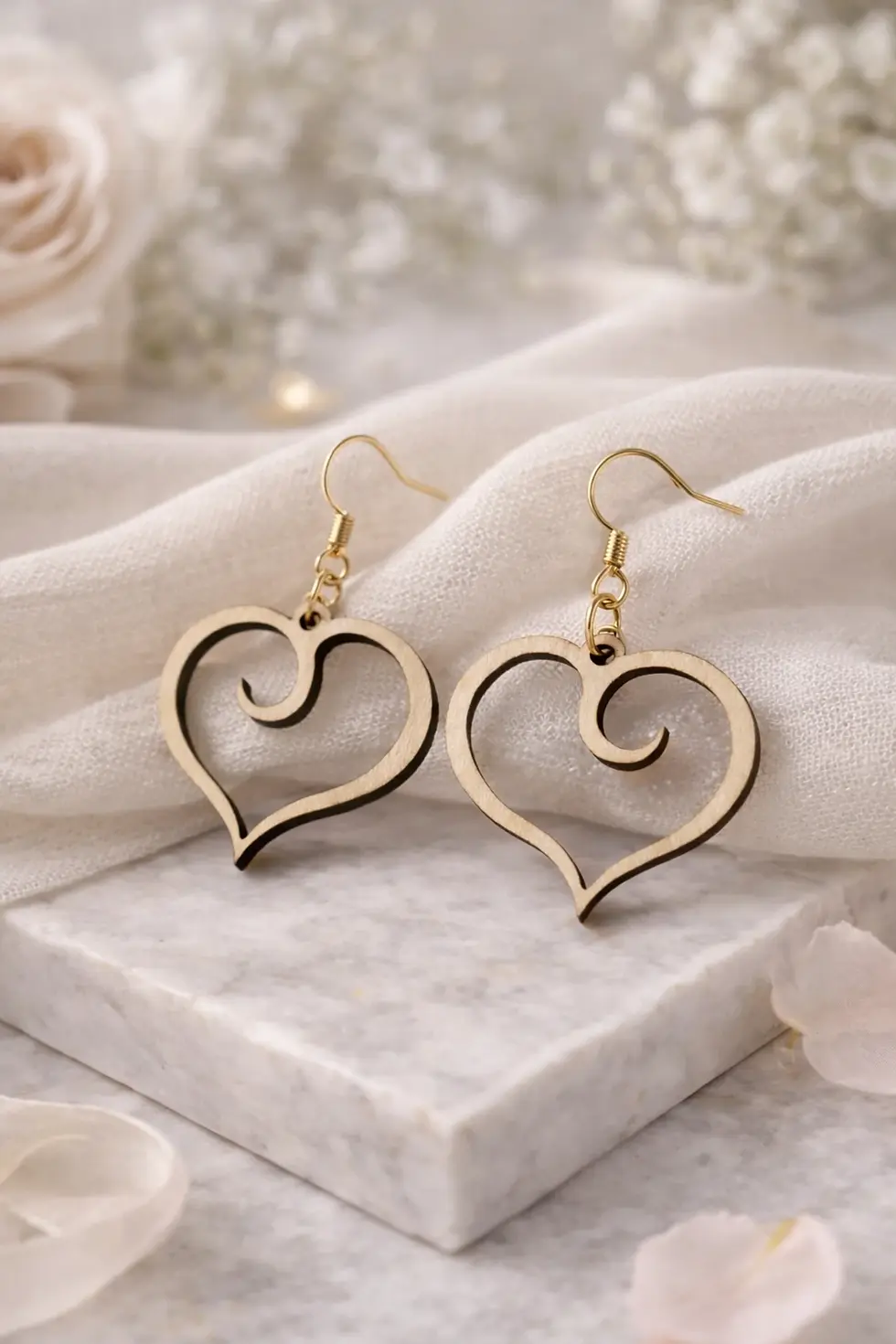 Élégantes boucles d'oreilles pendantes cœur en bois clair sur tissu blanc.
