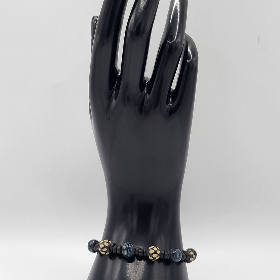 Bracelet en perles cuivrées sombre sur main mannequin noire.