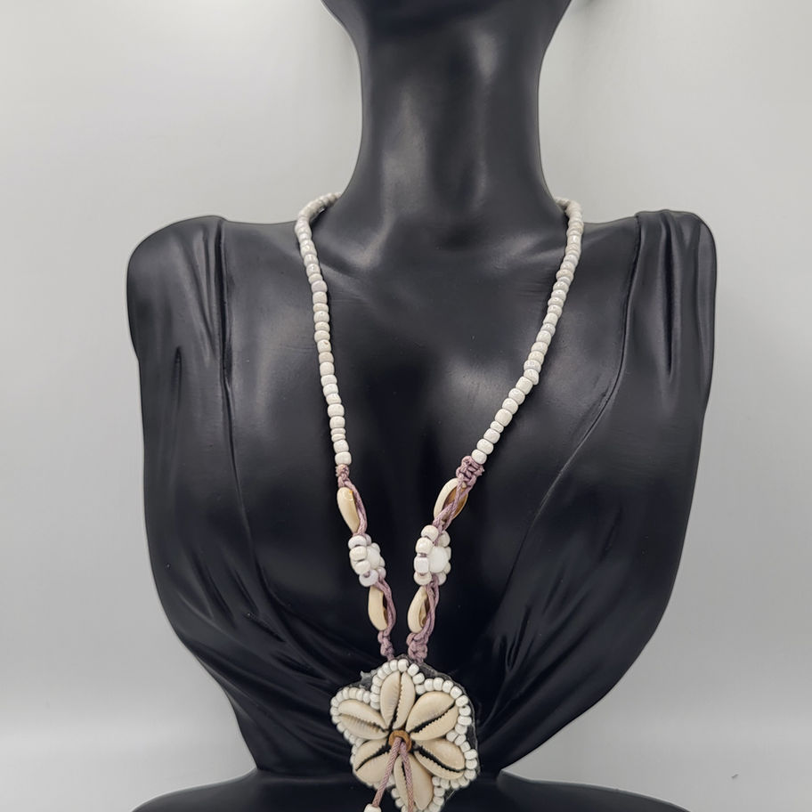 Collier de perles blanches avec pendentif floral et coquillage sur buste noir.