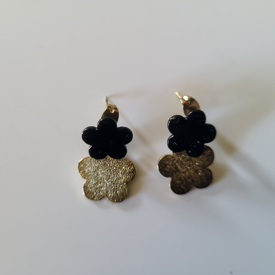 Boucles d'oreilles pendantes doubles fleurs, noires et dorées, sur fond blanc.