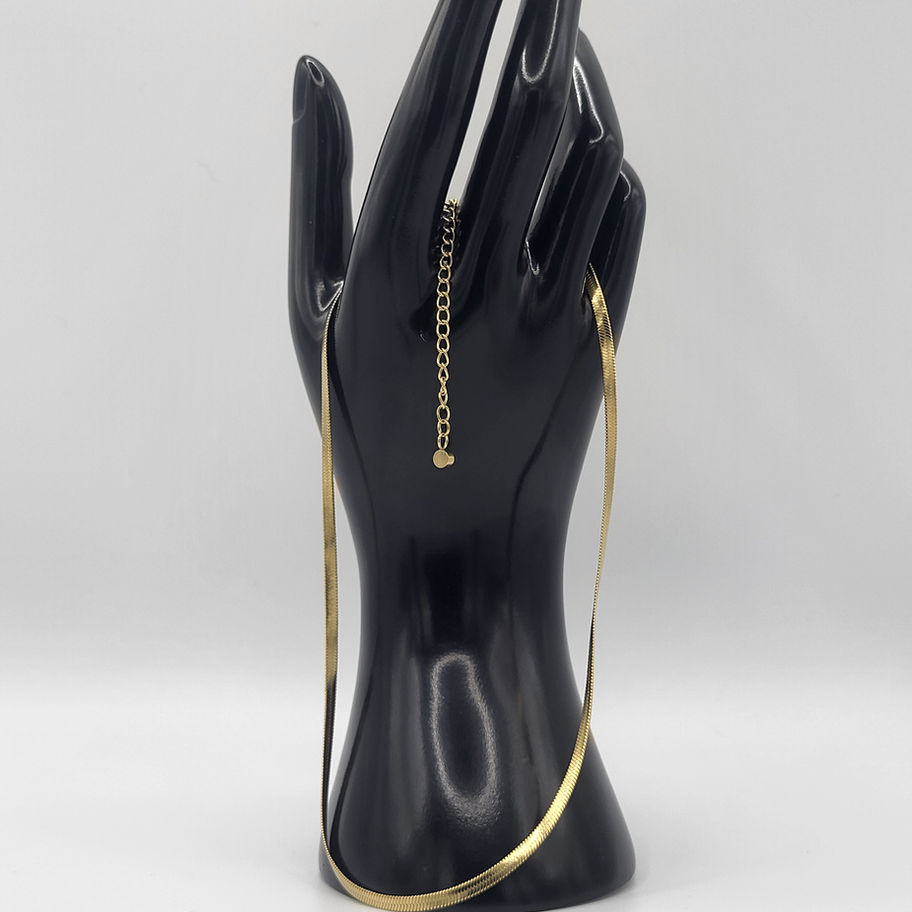 Chaîne dorée délicate présentée sur une main de mannequin noire.