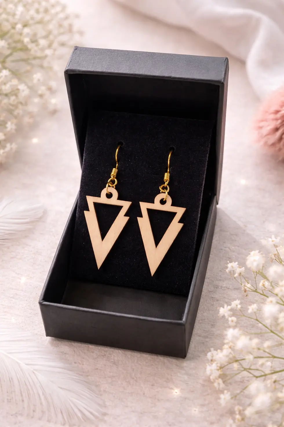 Boucles d'oreilles triangulaires géométriques en bois clair dans boîte cadeau noire.