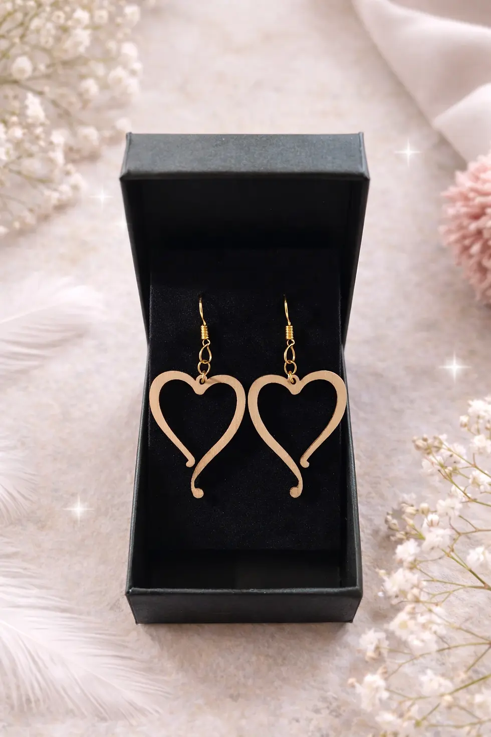 Paire de boucles d'oreilles cœur dorées dans une boîte cadeau noire ouverte.