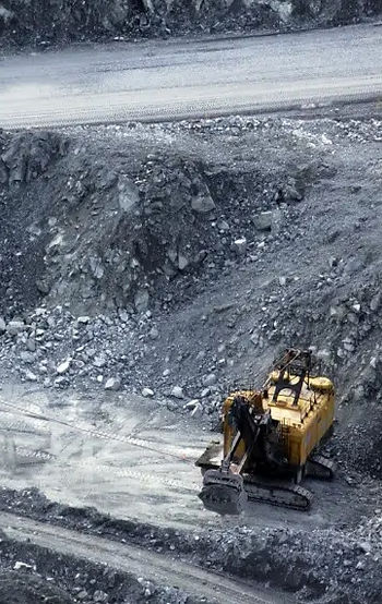Yellow excavator on a rocky terrain, working in a quarry background.