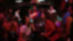 Crowd enjoying a concert in a dimly lit venue. A guitarist sings on stage, colorful lights illuminate the lively audience below.