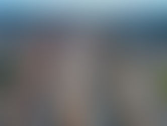 Aerial view of a highway under construction with cars and trucks. Surrounding landscape includes desert, buildings, green field, and mountains.