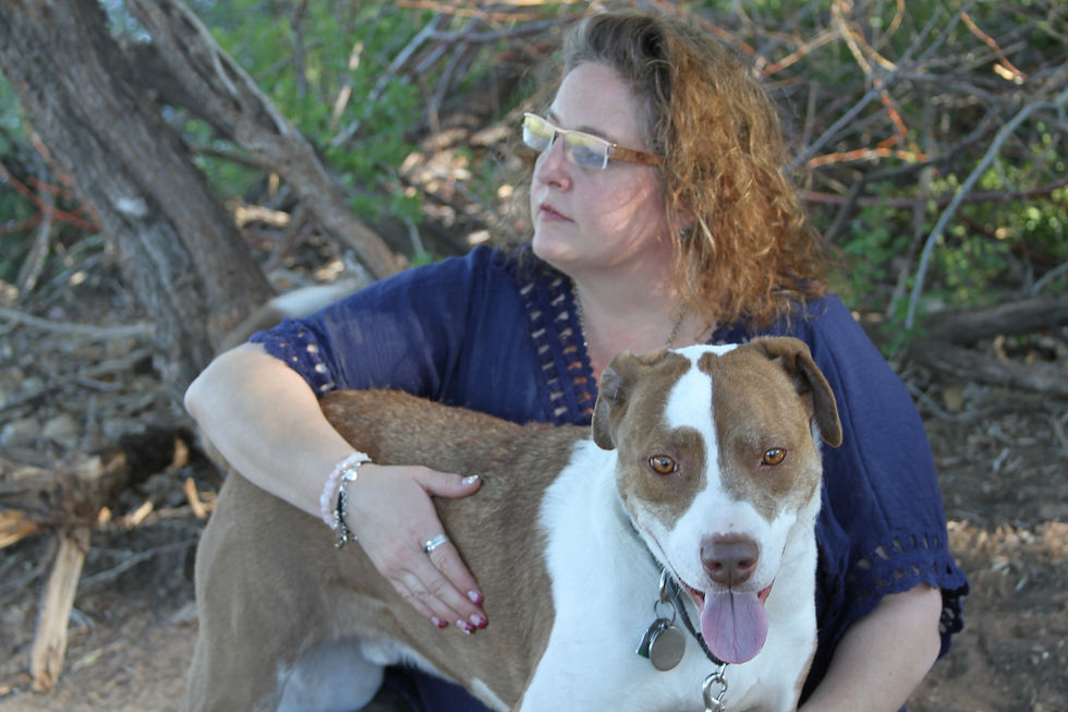 Stephanie sitting outside looking in the distance. Her brown and white dog Treun is standing in front of her looking a the camera, tongue showing.