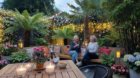 Tropical Brixton garden by Stuart Savage Landscaping with oak sleeper walls, lush jungle planting and two ladies enjoying drinks in the daytime in a South London garden