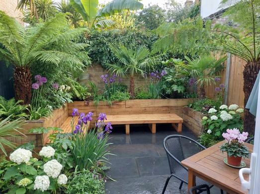 A lush garden oasis featuring Midnight Black Limestone Paving from London Stone Garden Brixton, beautifully accented with vibrant greenery and vibrant blossoms, creating a serene outdoor retreat.