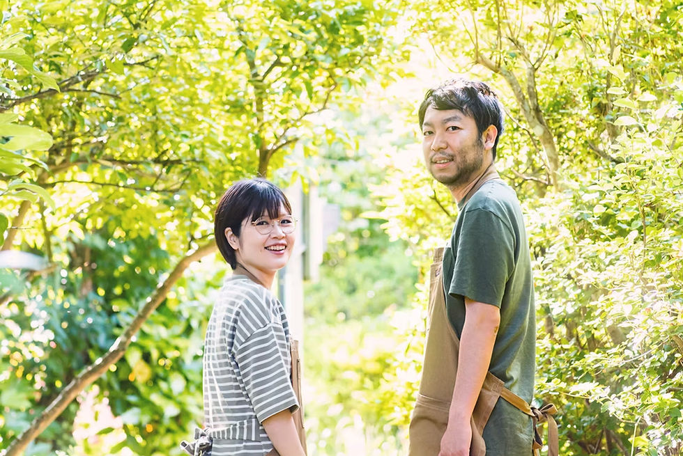 笑顔の男女が並んで立つ、木々の緑を背景に。ハマダノブヒロも写っている。