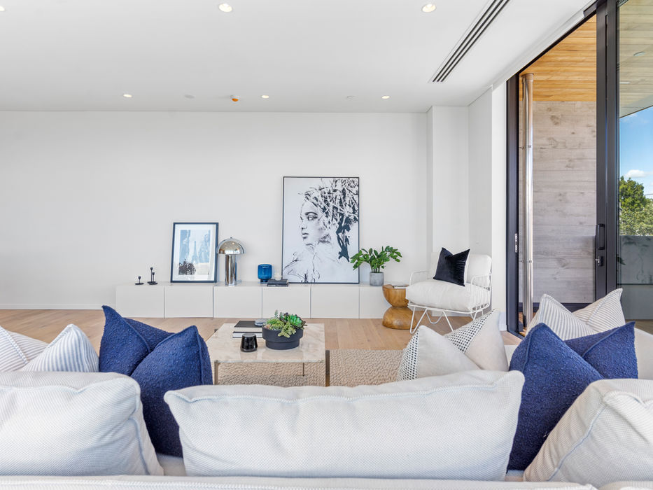 Modern living room with white walls, art, blue pillows, and open doors.