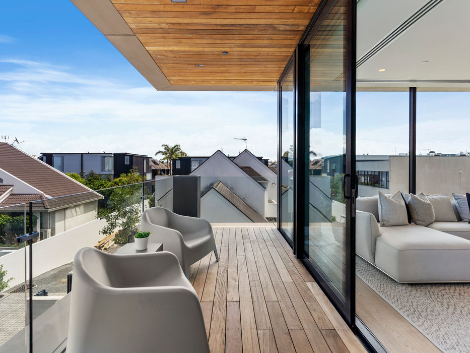Modern balcony with furniture, cityscape view, wooden deck, and glass doors.