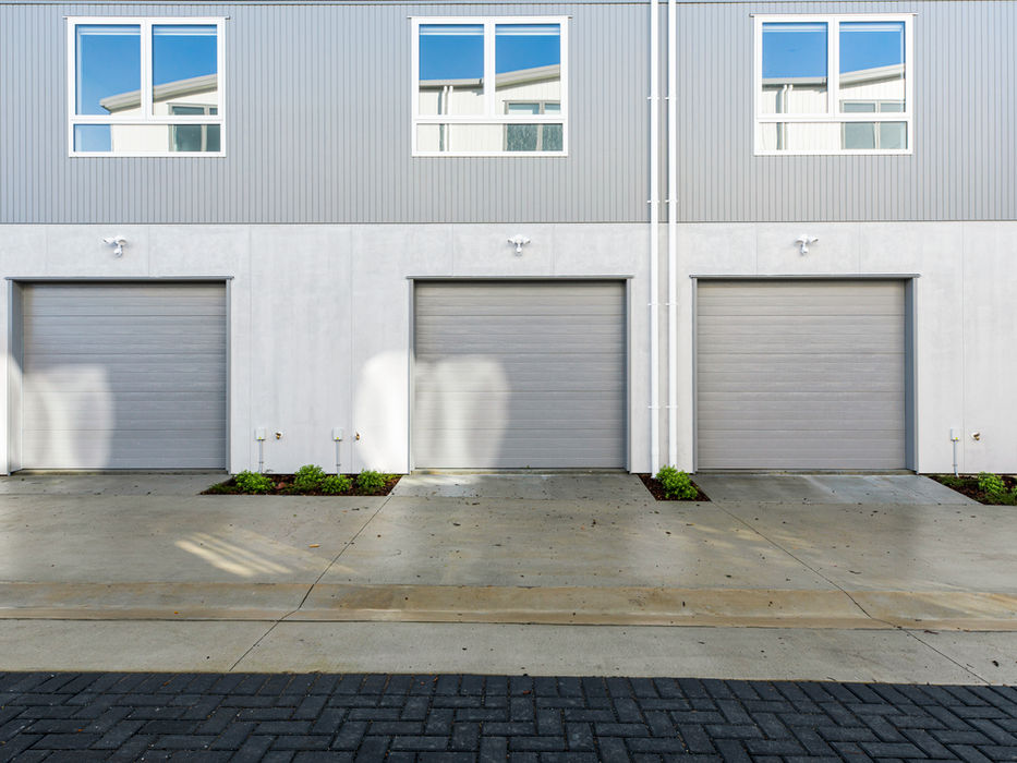 Modern townhouses with three gray garage doors and windows, exterior view.