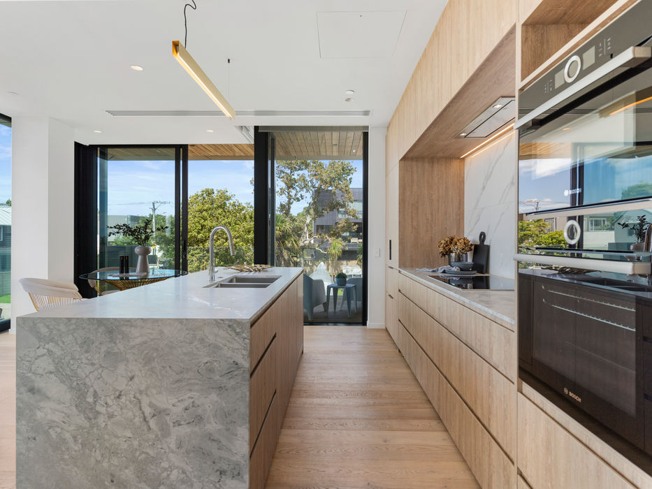 Modern kitchen with island, wooden cabinets, and large windows overlooking trees.
