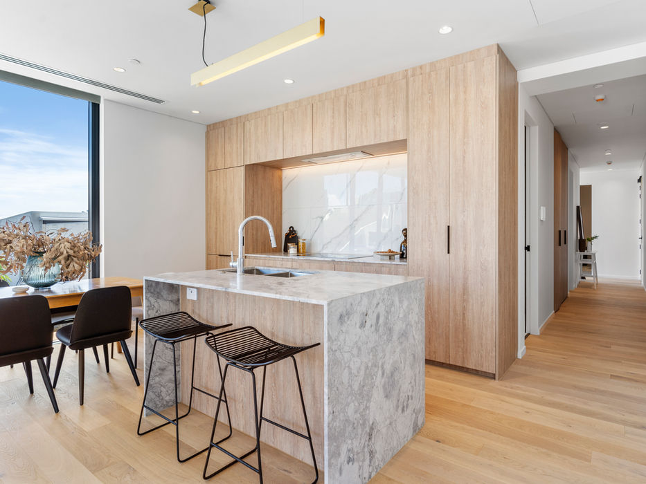 Modern kitchen with island, marble countertop, and wooden cabinets; dining table visible.
