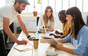 A diverse group of professionals collaborating around a bright office table, smiling and reviewing documents together, symbolizing teamwork, inclusion, and shared financial confidence.