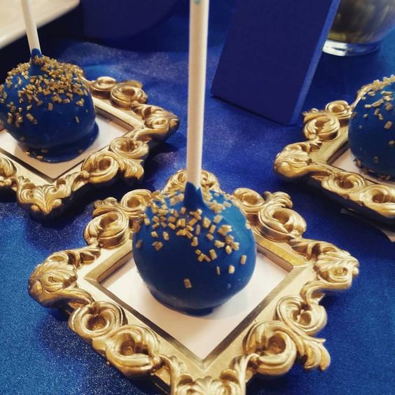 Blue cake pops with gold sprinkles on golden mini frames.