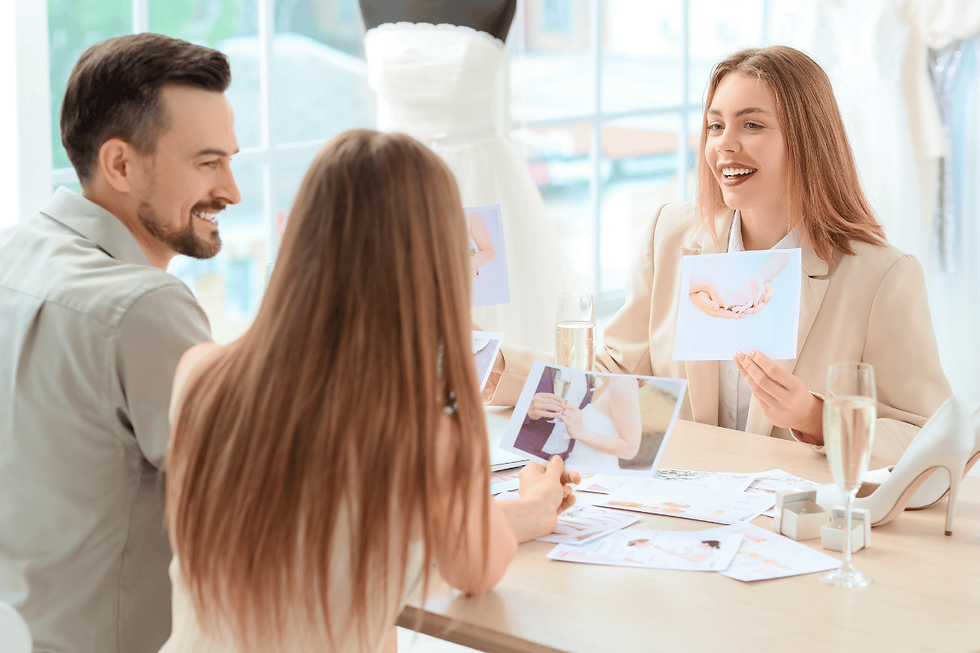 Tres personas sonrientes revisan fotos de boda en una mesa, con un vestido blanco al fondo y copas de champán.