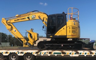 JET yellow sumitomo excavator being loaded on to truck