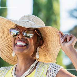 Smiling woman in sunglasses and straw hat, adjusting brim. Sunny outdoor setting with trees. Text: "The Bedrock Group" on bottom.