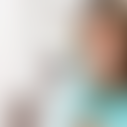 Smiling woman with curly hair in a turquoise shirt holding glasses, in a bright office. Text: TBG Advisors Medicare FMO.