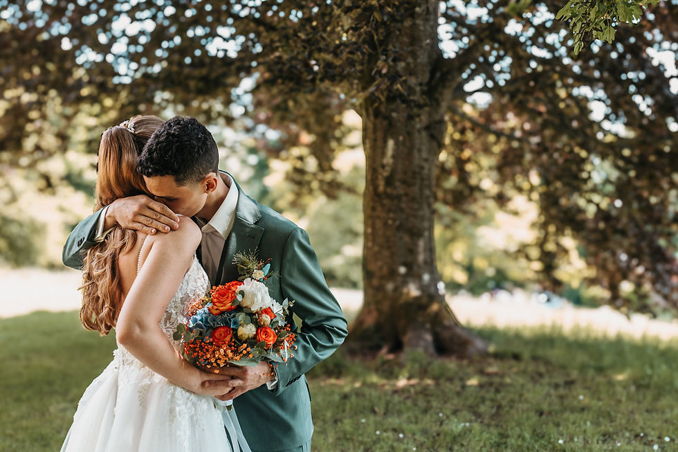 Glückliches Brautpaar umarmt sich innig im Park mit buntem Blumenstrauß.