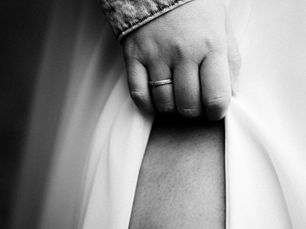 Schwarzweißaufnahme einer Hand mit Ring, die einen fließenden Stoff – vermutlich ein Kleid – leicht zusammenfasst; Detailaufnahme mit Fokus auf Textur und Stimmung.