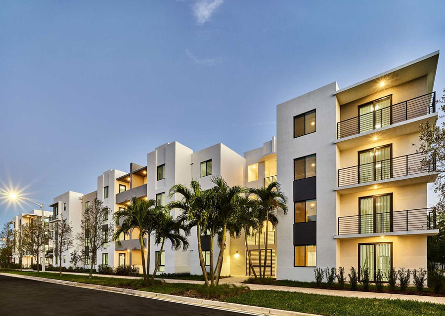 Four-story white apartment building with balconies and palm trees at dusk