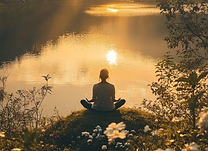 Person meditating beside a peaceful lake at sunrise to represent emotional regulation and creating a calm state for change.