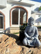 Escultura de Buda entre piedras y plantas del jardín interior; atmósfera de silencio y contemplación en Casa Ama Nacer.