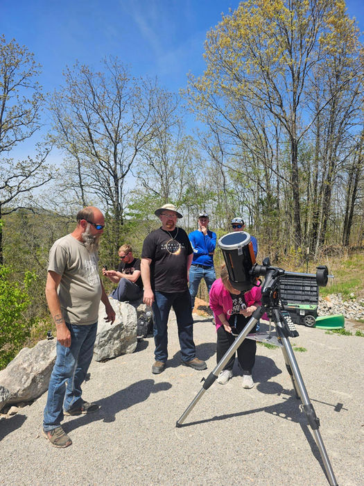 An image of the total solar eclipse at the river village with people observing from a telescope.