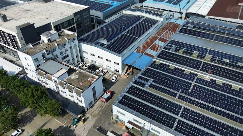 Aerial view of buildings with large solar panels on rooftops. Several white cars are parked below, and lush green trees line the street.