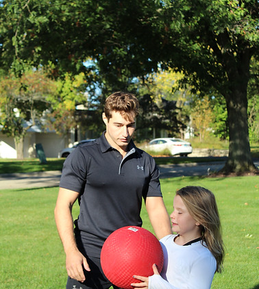 George Kostopoulos coaching a young girl with a red exercise ball outdoors