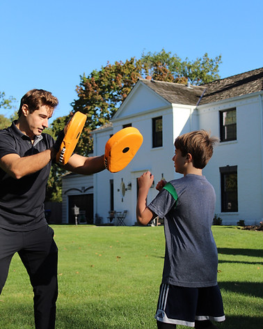 George Kostopoulos holding boxing pads for a young client during an outdoor training session