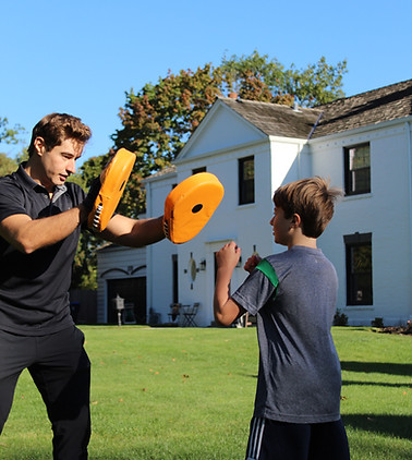 George Kostopoulos holding boxing pads for a young client during an outdoor training session