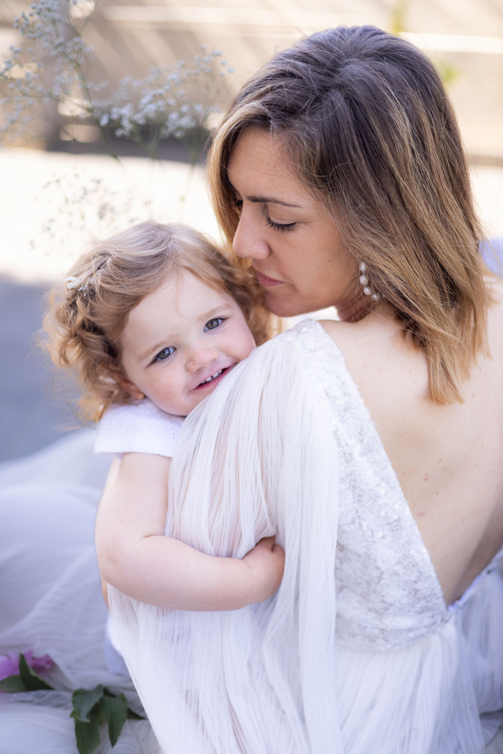Future mariée en plein essayage robe de mariée Var, de trois-quarts devant un grand miroir dans une boutique lumineuse et moderne du sud de la France, robe blanche fluide avec dentelle délicate mise au point, conseillère ajustant le dos de la robe, décor méditerranéen élégant en arrière-plan flou.