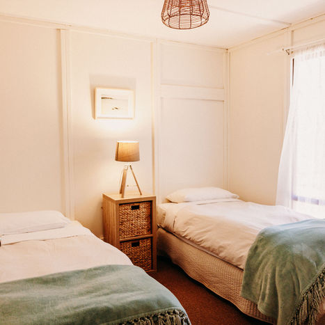 Timber cottage bedroom with two single beds, two drawers and window facing out to exterior of cottage